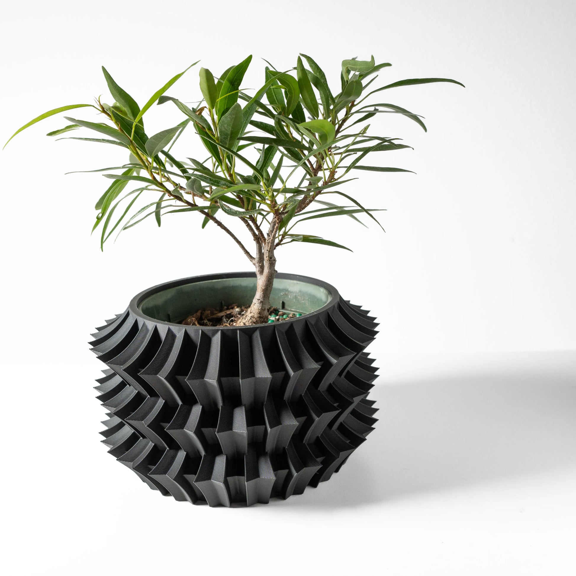 Pot décoratif noir en plastique moderne avec motif géométrique tridimensionnel, accueillant une plante verte à feuilles.