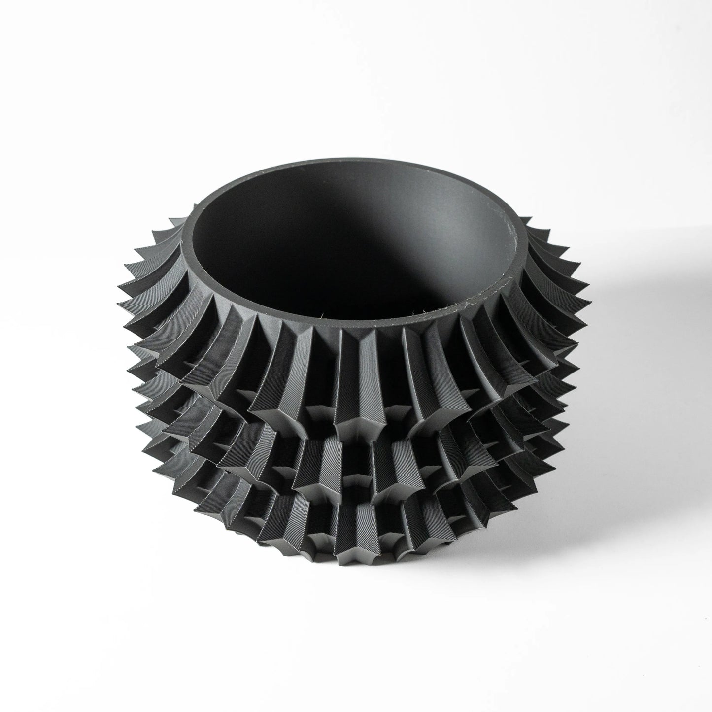 Pot décoratif noir mat avec structure géométrique épaisse en relief, forme cylindrique à bords arrondis.