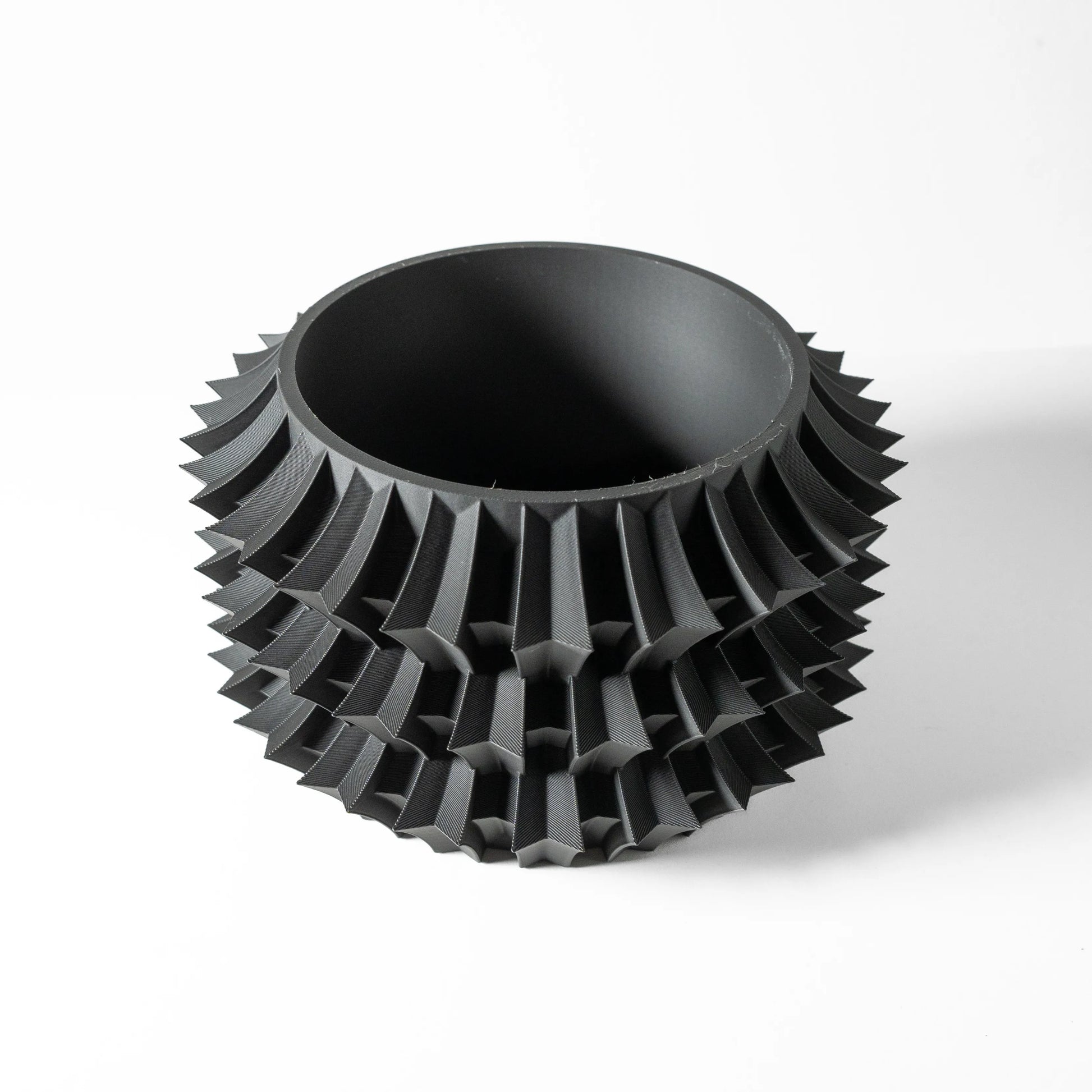 Pot décoratif noir mat avec structure géométrique épaisse en relief, forme cylindrique à bords arrondis.