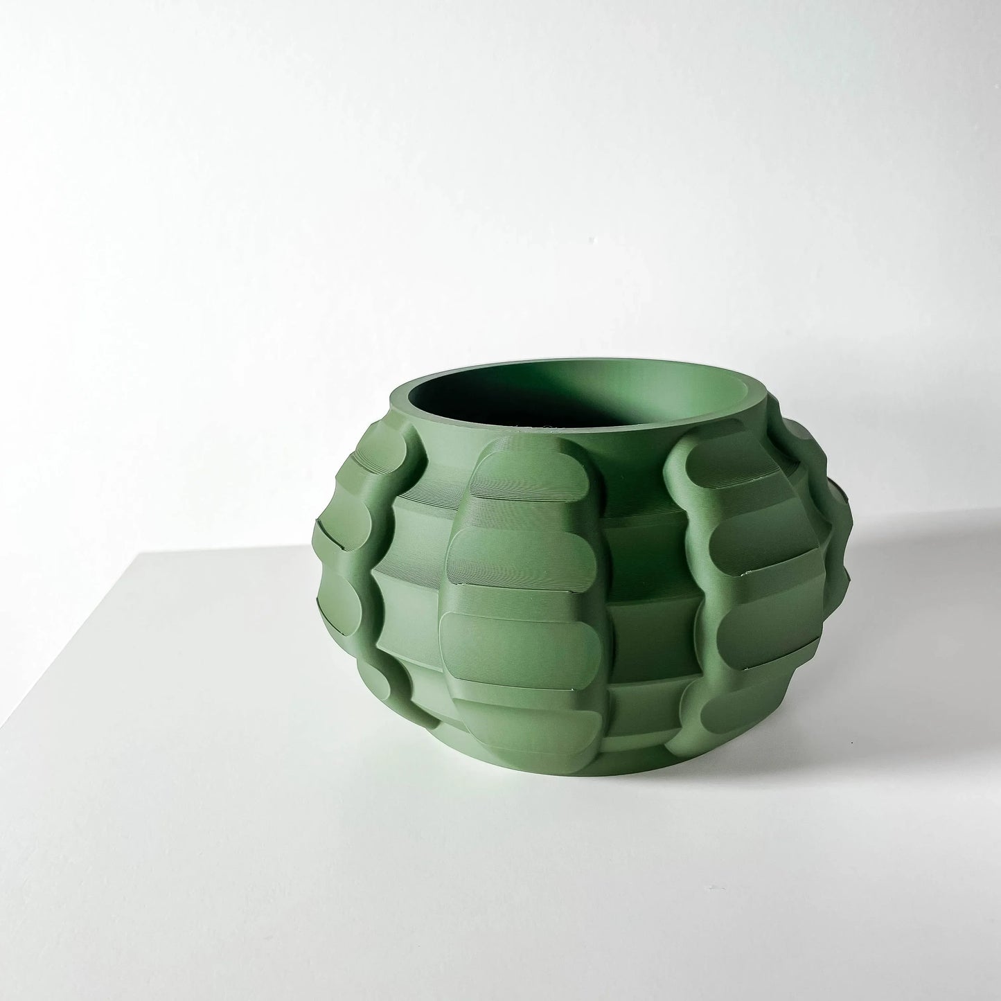 Pot décoratif rond vert foncé avec surface striée en relief formant des motifs ondulés, finition mate, style contemporain.