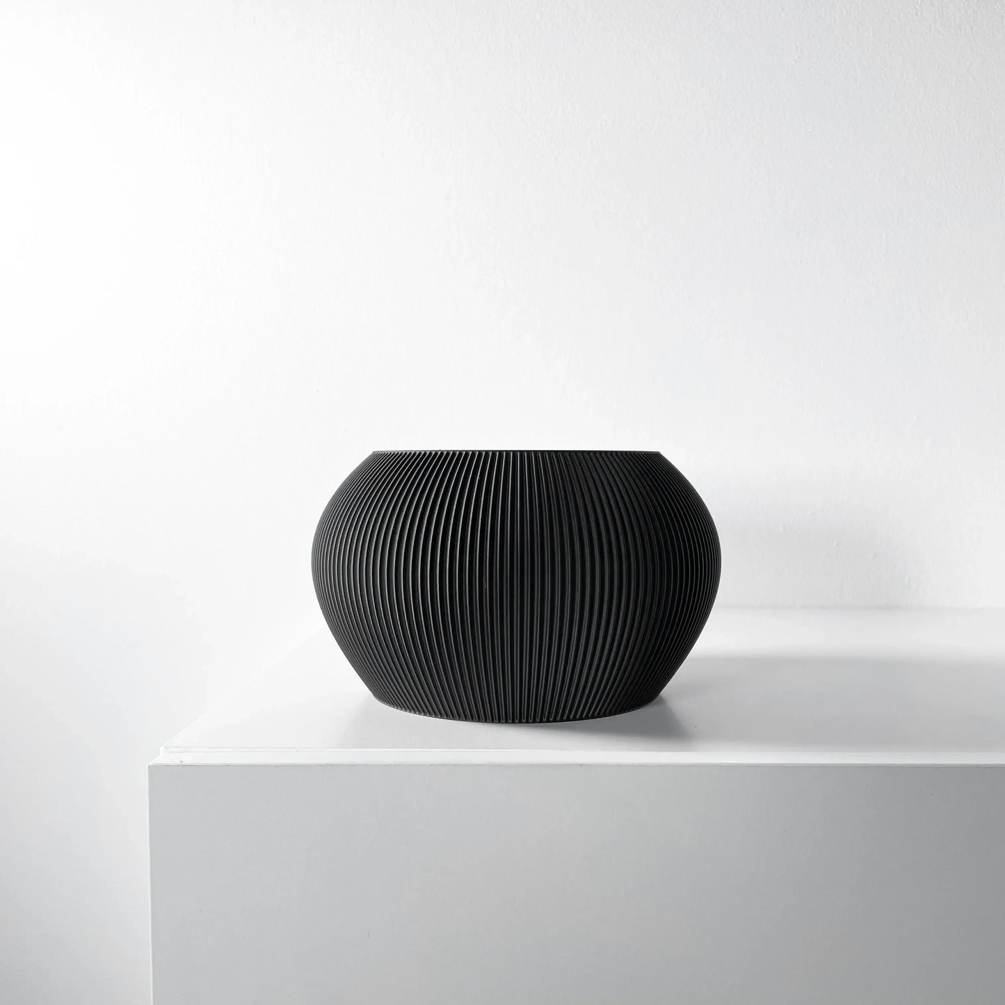 Pot décoratif noir mat, forme ronde bombée avec surface texturée rayée verticale, style moderne.