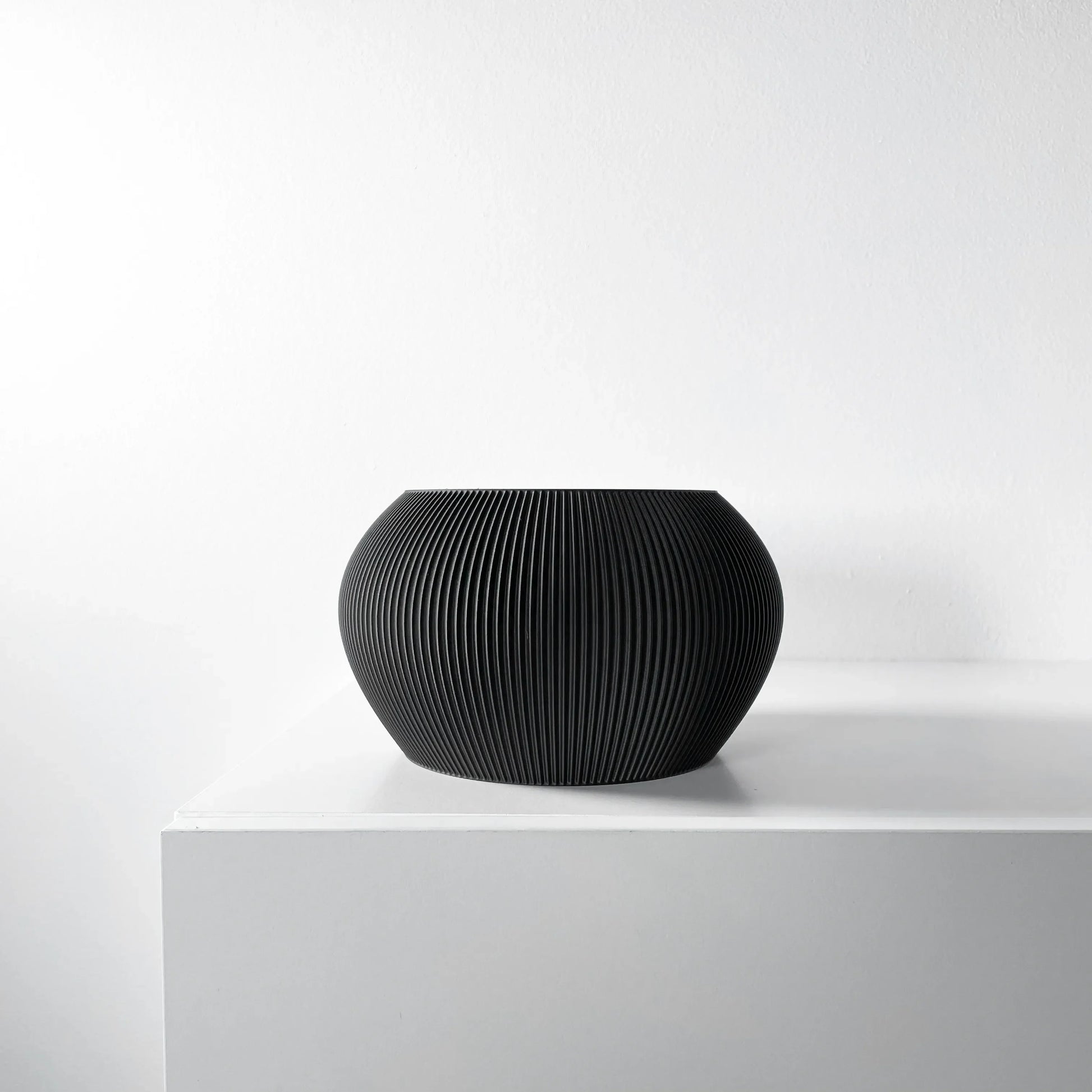 Pot décoratif noir mat, forme ronde bombée avec surface texturée rayée verticale, style moderne.