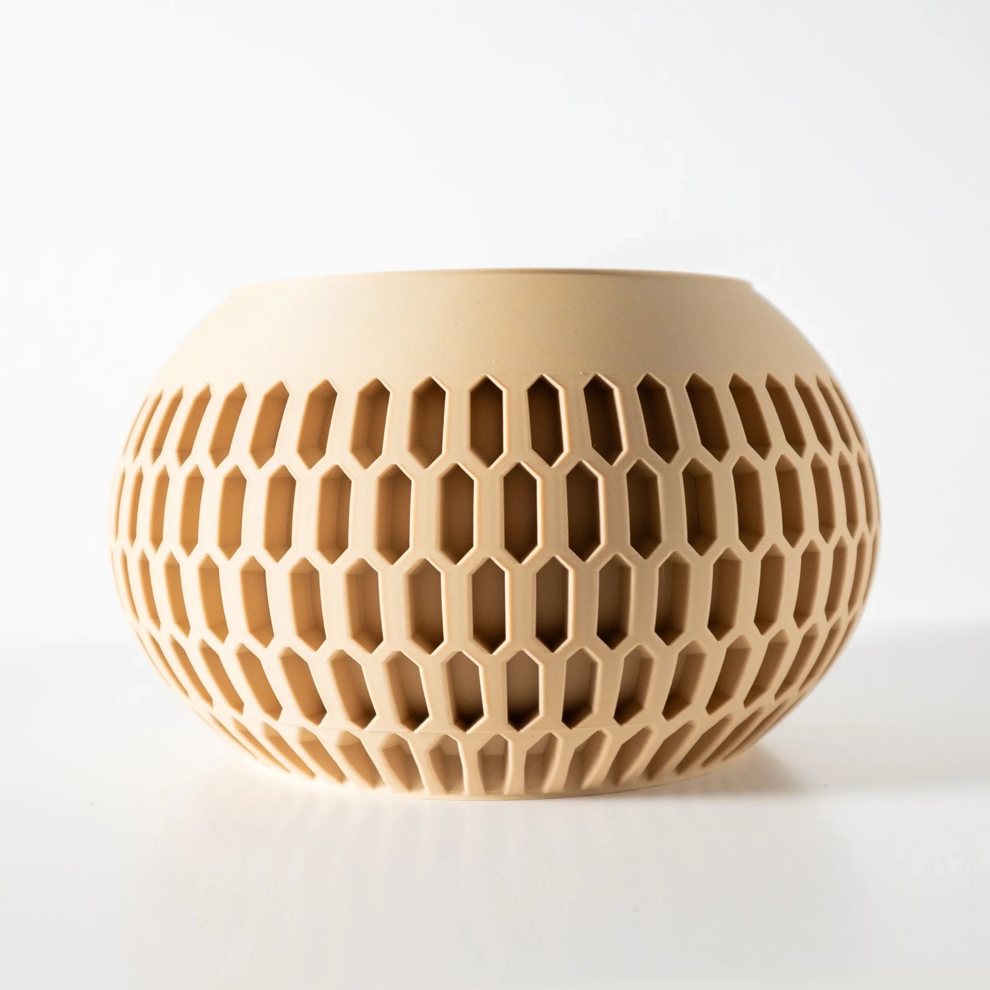 Pot décoratif beige en plastique moderne, forme ronde avec motif hexagonal ajouré sur toute la surface.