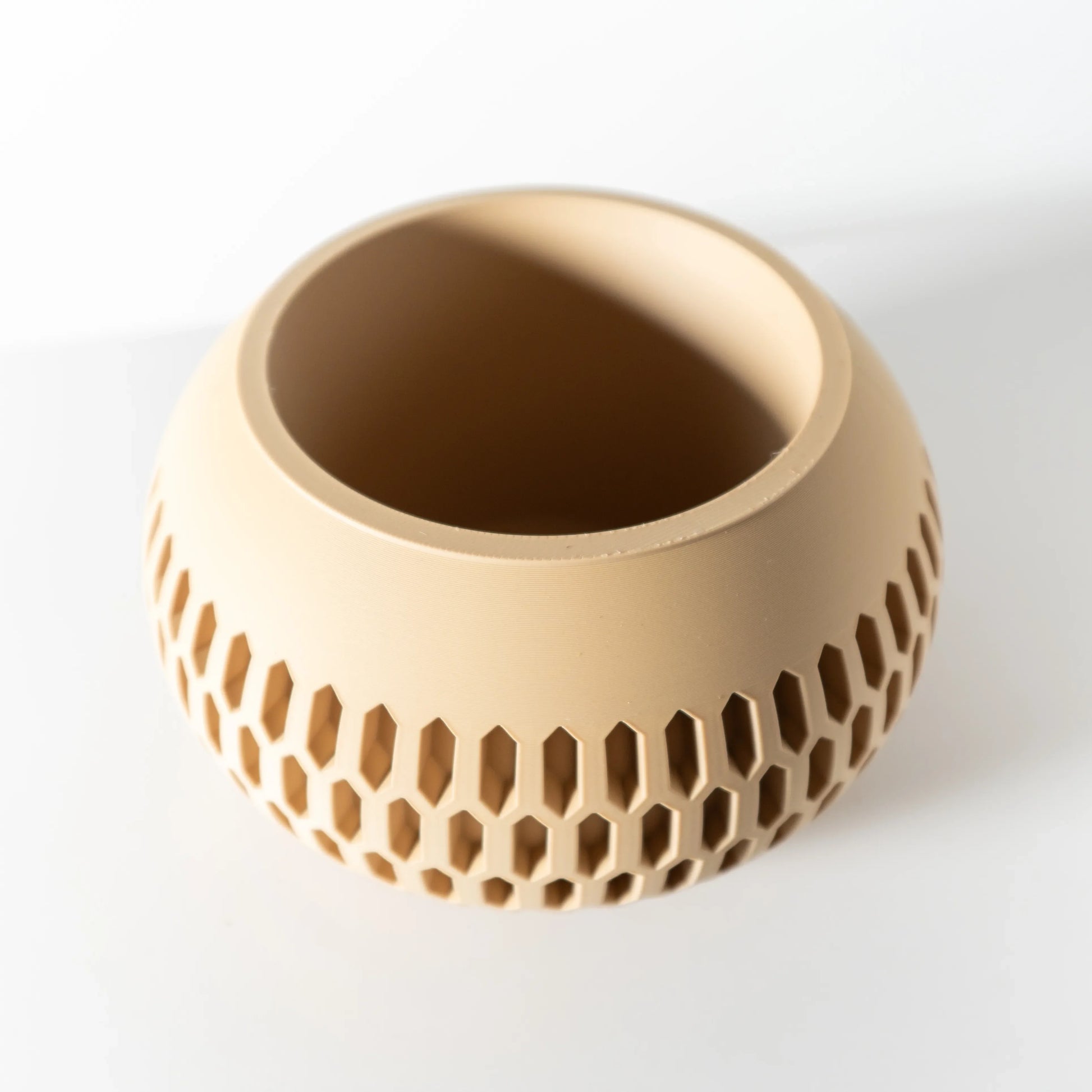Pot décoratif beige en matière translucide avec motifs hexagonaux ajourés sur toute la surface inférieure, forme ronde.