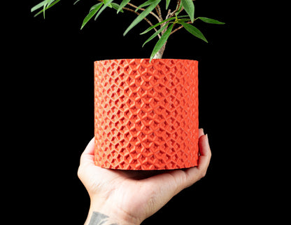 Pot décoratif Ordan orange en matériau durable avec surface texturée en motif géométrique contemporain, tenue à la main.