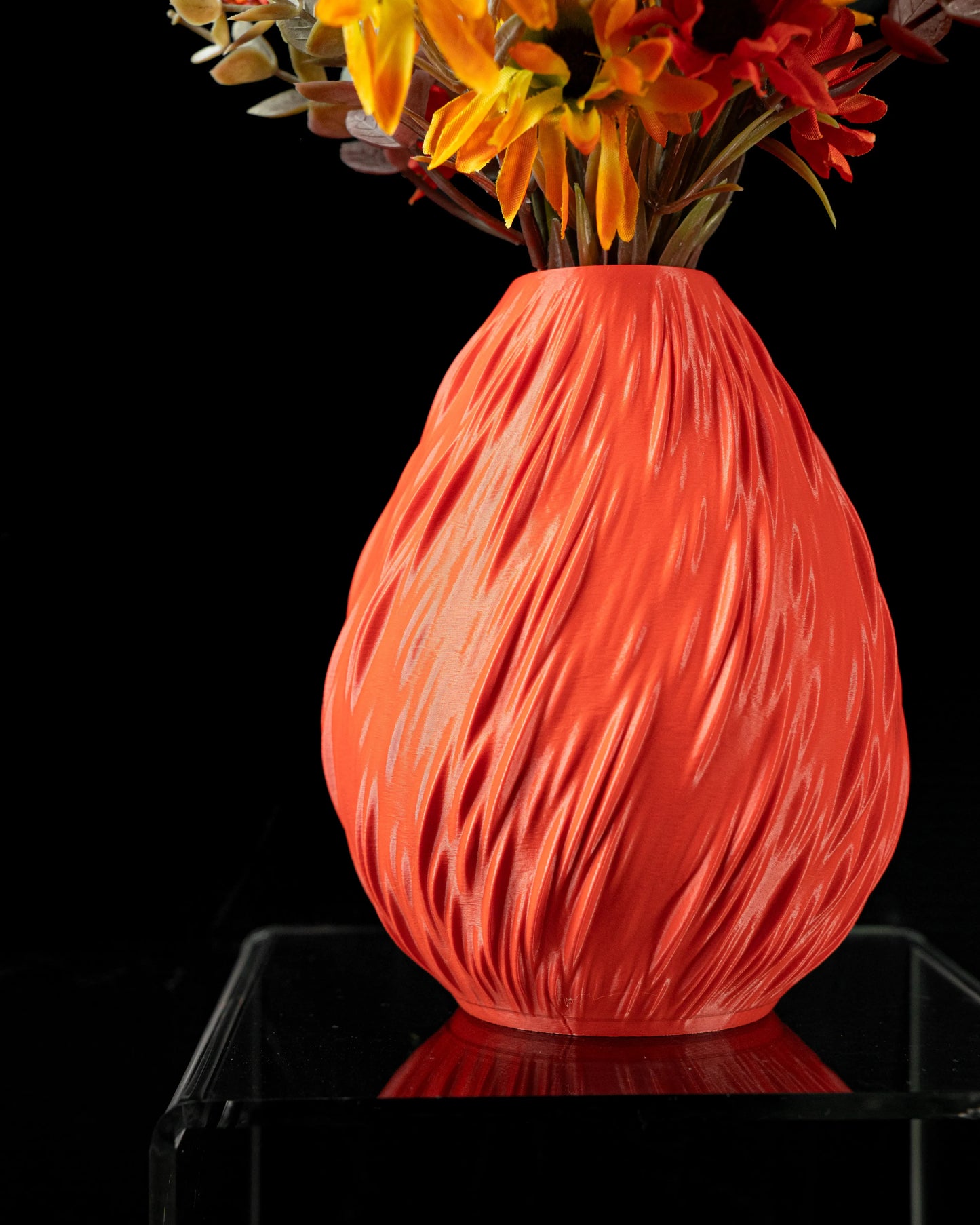 Vase ovale rouge texturé avec motifs en relief ondulés, finition mate, posé sur une surface noire brillante.