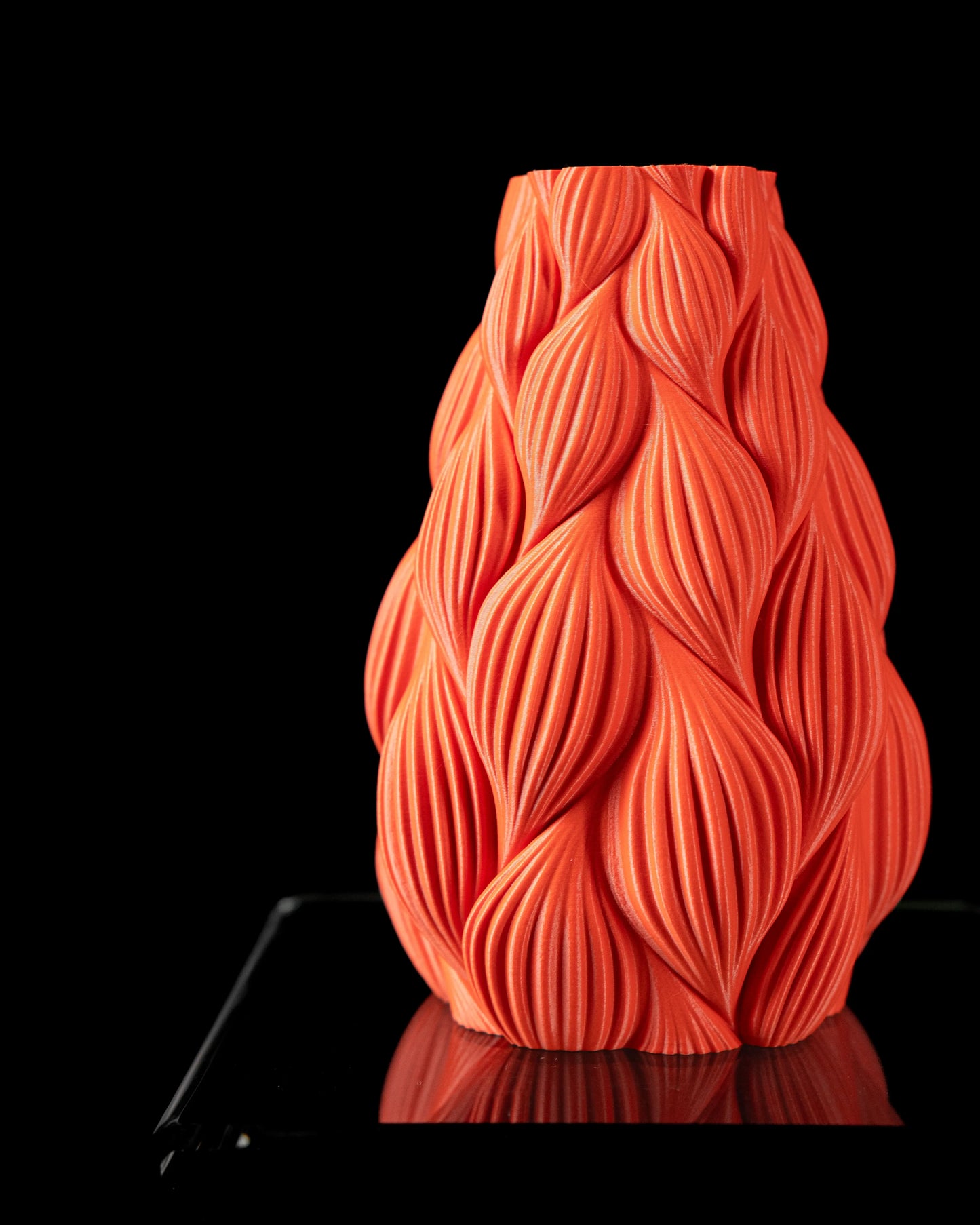 Vase orange vif en matériau mat avec motif ondulé en relief rappelant des feuilles stylisées, forme élancée et large à la.