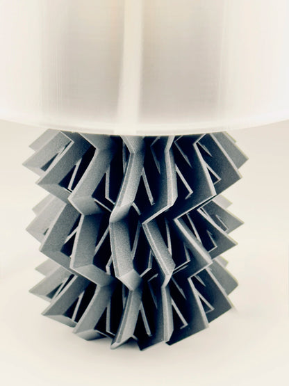 Socle noir mat en plastique durable formant une structure géométrique contemporaine sous abat-jour translucide.